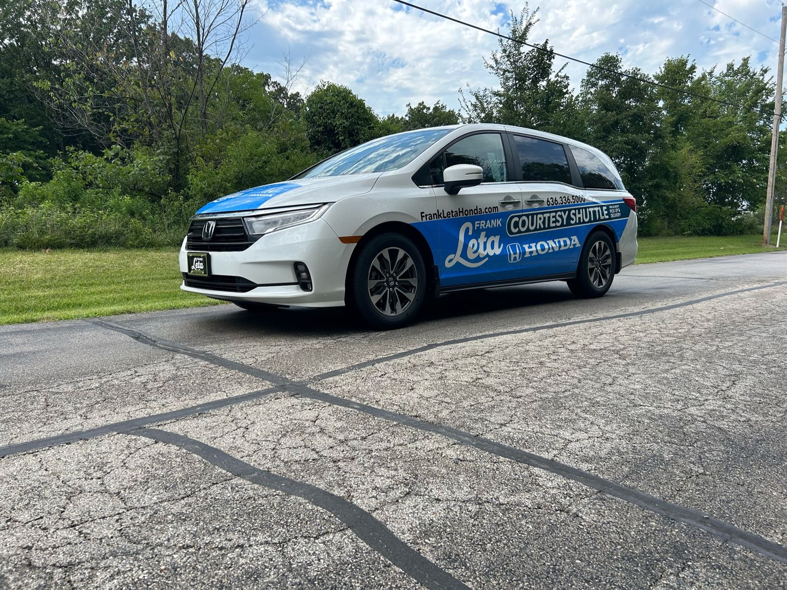 A Honda Odyssey courtesy shuttle with a partial wrap: the store's name, website and phone number