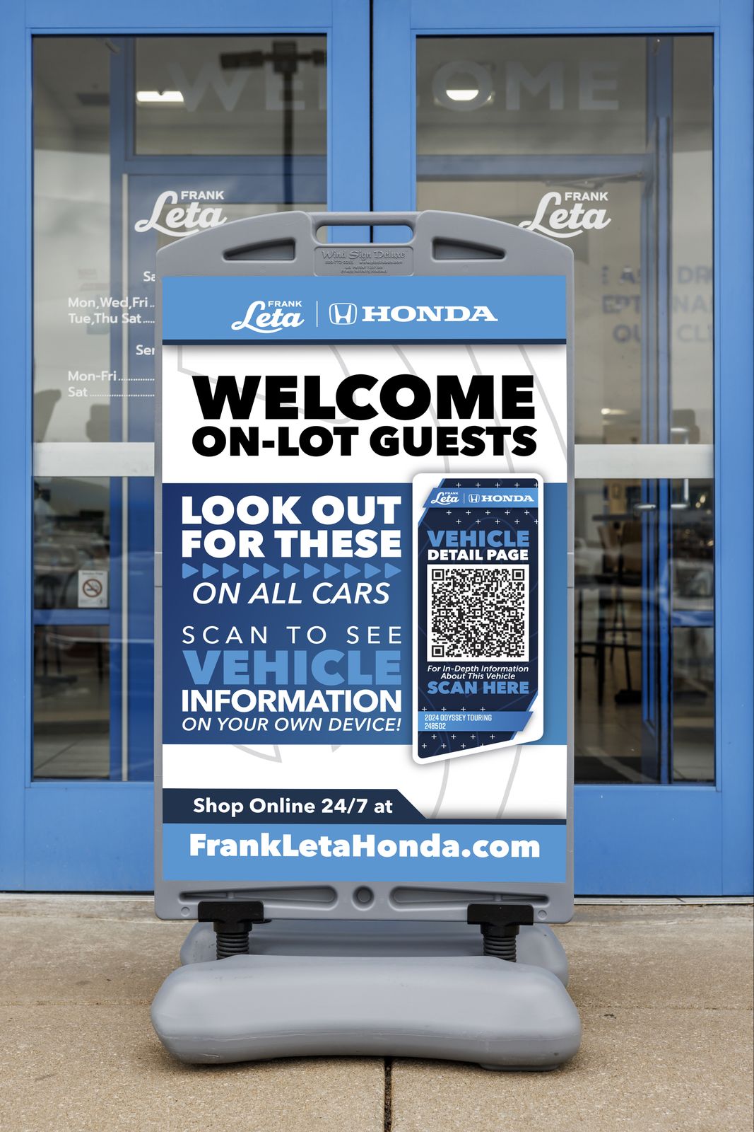 A wind sign at Frank Leta Honda's front door reading Welcome on-lot guests: look out for these on all cars, scan to see vehicle information, with the QR placard shown on it
